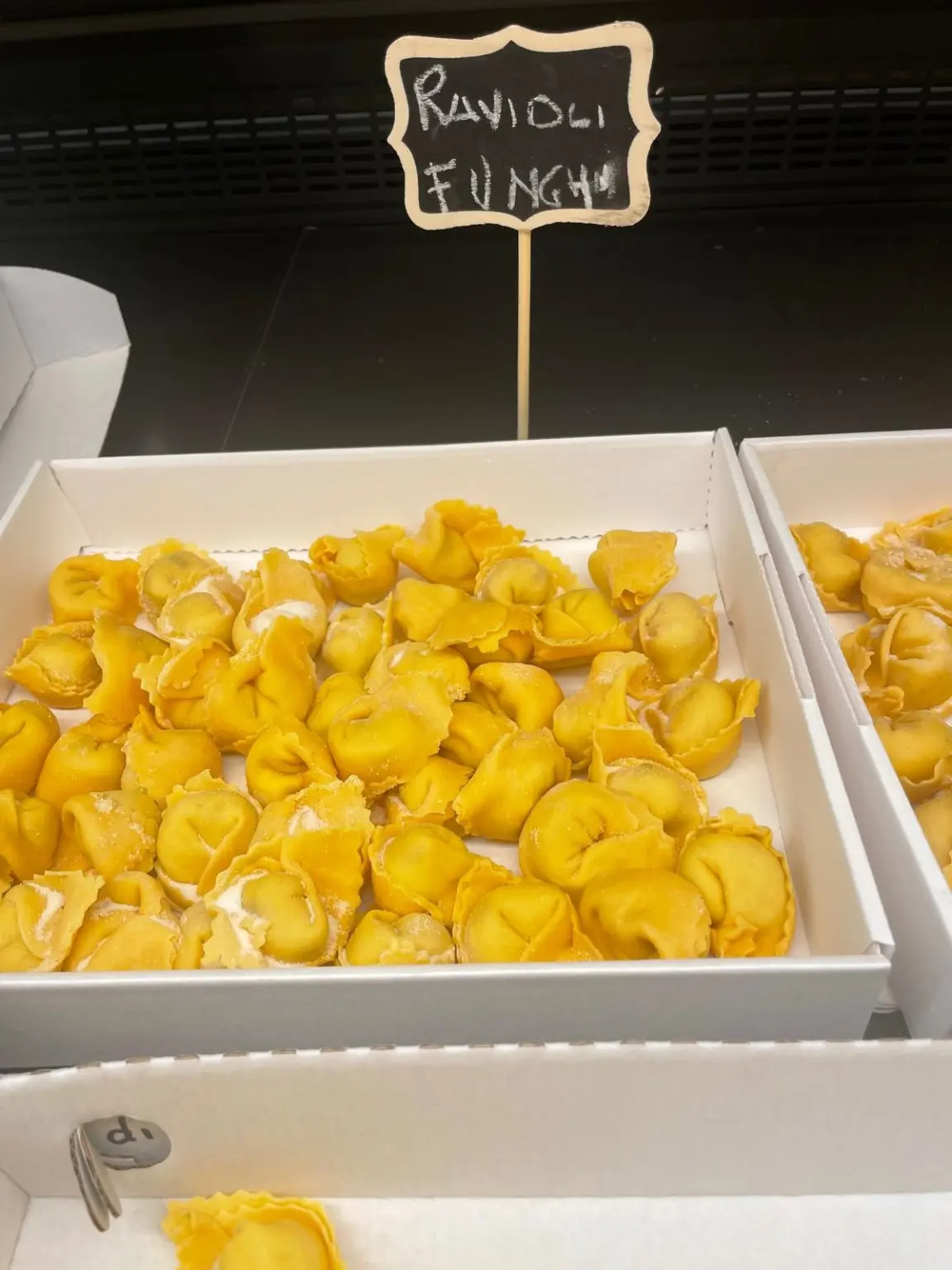 Ravioli ai funghi in una cassetta del banco, con lavagnetta scritta a mano